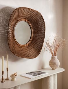 a round mirror hanging on the wall above a white table with candles and vases