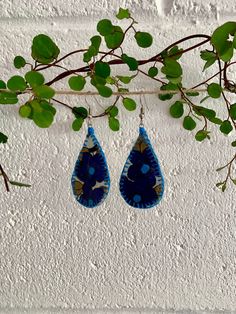 two blue tear shaped earrings hanging from a branch with green leaves in front of a white wall