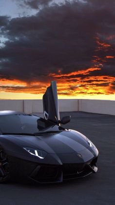 a black sports car parked on top of a parking lot next to the ocean at sunset