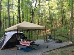 a tent set up in the middle of a wooded area with picnic tables and chairs