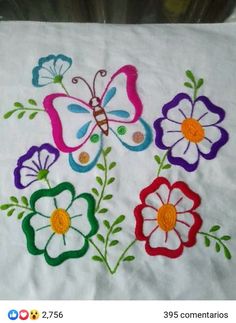 a white table cloth with colorful flowers and a butterfly on the center, embroidered onto it