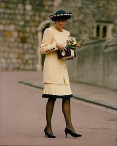 a woman in a yellow dress and black hat is holding a flower bouquet while walking down the street