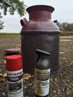 two spray cans sitting on the ground next to a metal container with rust - colored paint