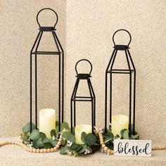 three black metal lanterns with candles and greenery on the floor next to a sign that says blessing