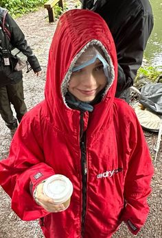 a young boy in a red jacket holding a cup of coffee