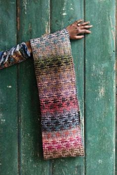 a person's hand is reaching out from behind a green wooden door with a multicolored scarf hanging on it