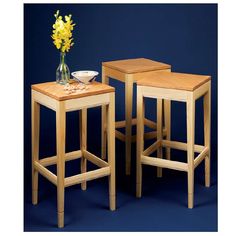 two wooden stools and a small table with flowers in the vase on top, against a blue background