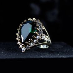 a ring with an oval shaped green stone surrounded by small white diamonds on a black surface