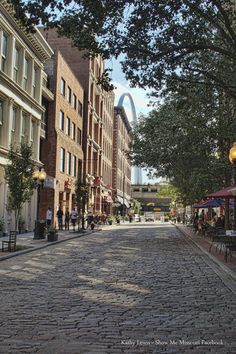 a cobblestone street with people walking on it and the arch in the background