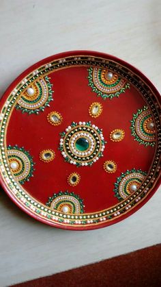 a red plate with gold and green designs on the bottom is sitting on a table