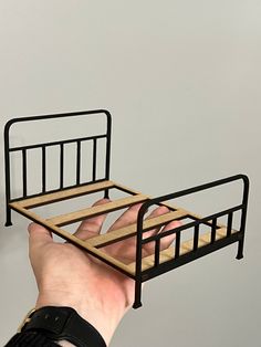 a hand holding a metal bed frame with wooden slats on it, against a gray wall