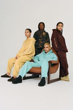 four people sitting on a chair in front of a white background, one person is wearing a yellow sweatshirt and the other wears a brown hoodie