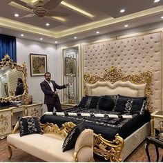 a man standing in front of a bed with black and gold decor on it's headboard