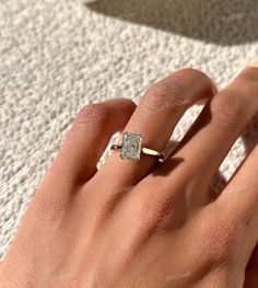 a woman's hand with a diamond ring on top of her finger, in front of a white carpet