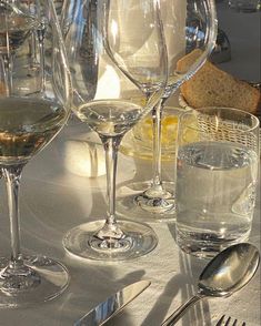 there are many wine glasses on the table with silverware next to them and bread