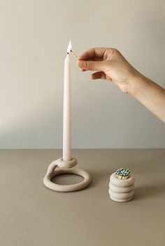 a person holding a candle in front of a stack of small white rings on top of a table