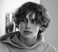 a black and white photo of a young man with curly hair wearing a hoodie