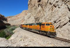 an orange and black train traveling through a canyon