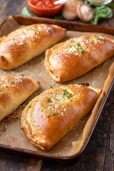 baked bread rolls on a baking sheet with garlic sprinkled on top and tomatoes in the background