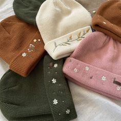 five knitted hats with flowers on them laying on a white sheet in the sun