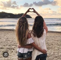 two girls making a heart shape with their hands on the beach