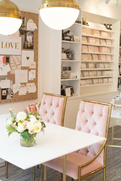 a white table topped with pink chairs next to a wall filled with cards and flowers