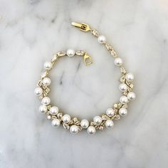 a bracelet with pearls and gold clasps on a marble surface, ready to be worn