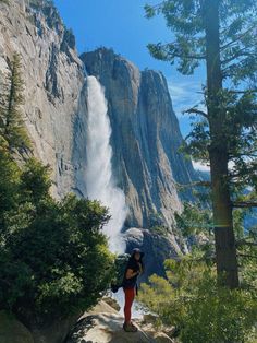 a person standing on top of a rock next to a tall mountain with a waterfall coming out of it