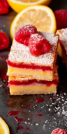 two pieces of cake with raspberries and powdered sugar on top next to sliced lemons