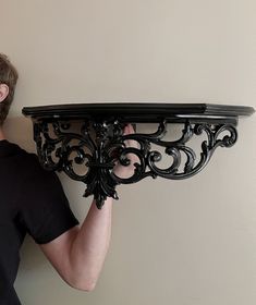 a man holding up a black shelf with an ornate design on the top and bottom