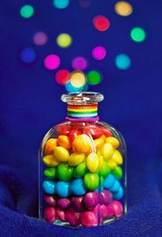 a glass jar filled with lots of colorful candies on top of a blue cloth