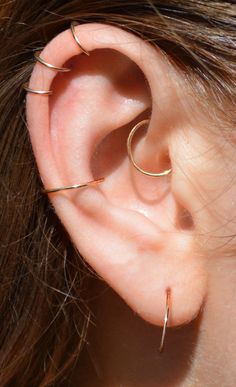 a close up of a person's ear with three thin gold hoops