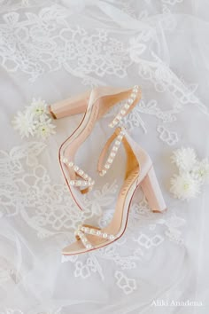 a pair of shoes with pearls on them sitting on top of a white lace covered surface