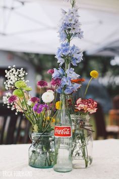 three glass jars filled with flowers sitting on top of a white tablecloth covered table