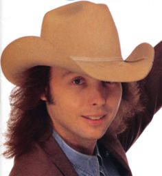 a man with long hair wearing a cowboy hat and holding his arm up in the air