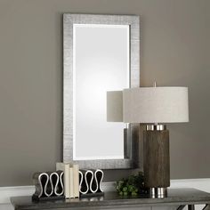 a table with a lamp, mirror and two books on it in front of a gray wall