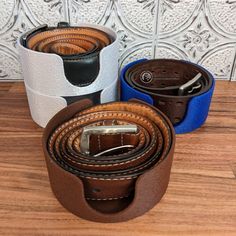 three leather belts sitting on top of a wooden table