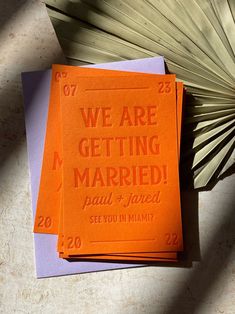 we are getting married cards on top of each other next to an orange paper fan