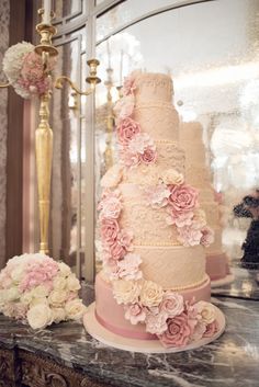 a three tiered wedding cake with pink flowers on the side and gold candelabra behind it