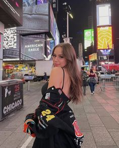 a beautiful young woman standing on top of a sidewalk in front of tall buildings at night