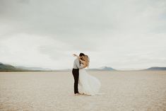 a bride and groom kissing in the middle of an empty desert field with mountains in the background