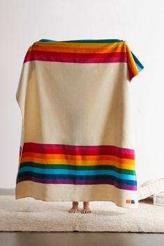 a person standing under a colorful blanket on top of a white bed covered in blankets