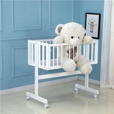 a white teddy bear sitting on top of a crib next to a blue wall