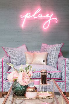 a pink neon sign above a blue couch and coffee table in a room with white carpet