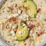 a white bowl filled with soup and topped with avocado