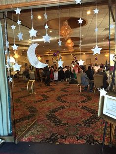 a room filled with people sitting at tables under stars and crescents hanging from the ceiling