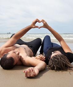 two people laying on the beach making a heart shape with their hands