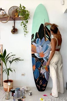 a woman standing next to a surfboard in a room with plants on the wall