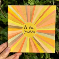 a hand holding up a small square painting with the words be the sunshine on it