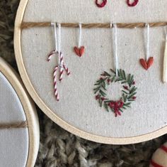 two hand embroidered christmas ornaments hanging on a wall next to a pair of scissors and yarn